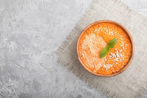 Carrot cream soup with sesame seeds in wooden bowl on a gray concrete background with linen textile