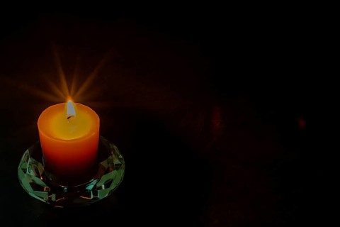 Burning candle in glass holder isolated on black textured background. Small amount of grain added