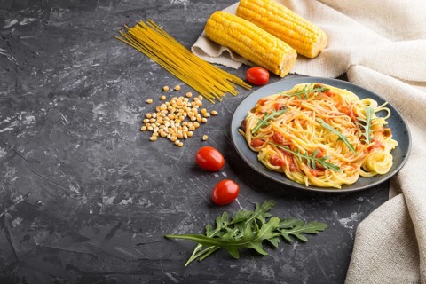 Corn noodles with tomato sauce and arugula on a black concrete background and linen textile. Side