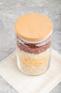 Glass jar with different kinds of rice poured in layers on a gray concrete background. side view,
