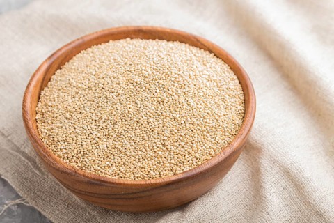 Wooden bowl with raw white quinoa seeds and wooden spoon on a gray concrete background and linen