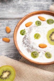 Yogurt with kiwi, gooseberry, chia and almonds in wooden bowl on gray wooden background and linen