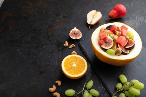 Vegetarian fruit salad of watermelon, grapes, figs, pear, orange, cashew on slate board on a black