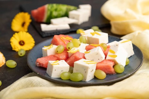 Vegetarian salad with watermelon, feta cheese, and grapes on blue ceramic plate on black concrete