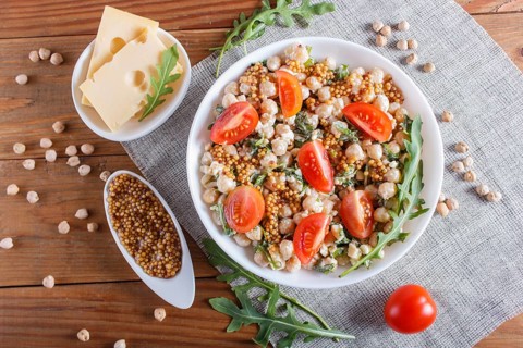 Vegetarian salad of boiled chickpeas, cheese, arugula, mustard and cherry tomatoes on brown wooden