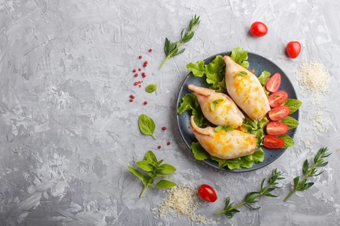 Stuffed baked squid with greens on a blue ceramic plate on a gray concrete background, top view,