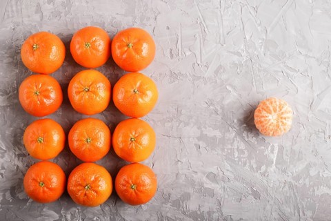 Rows of tangerines forming a rectangle and one peeled tangerine on a gray concrete background, top