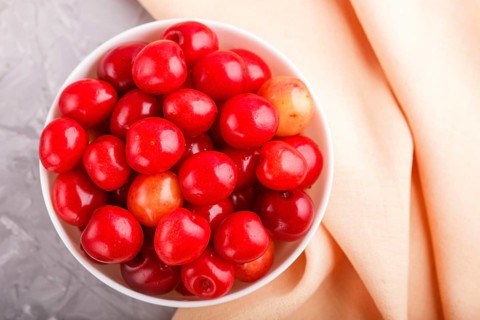 Fresh red sweet cherry in white bowl on gray background with orange textile. top view, flat lay