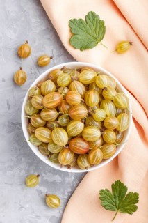 Fresh green gooseberry in white bowl with orange textile on gray concrete background. top view,