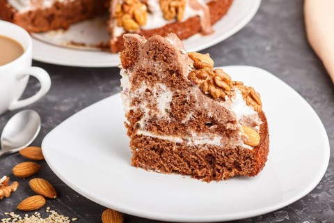 Homemade cake with milk cream, cocoa, almond, hazelnut on a black concrete background and a cup of