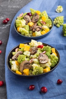 Vegetarian salad from romanesco cabbage, champignons, cranberry, avocado and pumpkin on a black