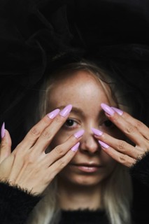 A striking image of a young blonde caucasian woman with purple nails covering her face with both