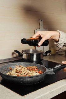 Unrecognizable woman pouring oyster sauce into noodles in a frying pan
