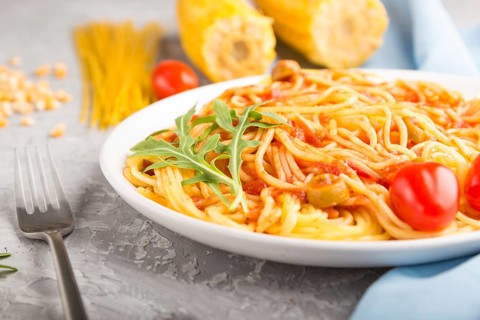 Corn noodles with tomato sauce and arugula on a gray concrete background and blue textile. Side