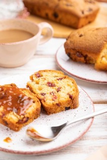 Homemade cake with raisins, almonds, soft caramel and a cup of coffee on a white wooden background.