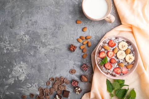 Chocolate cornflakes with milk, strawberry and almonds in ceramic bowl on gray concrete background