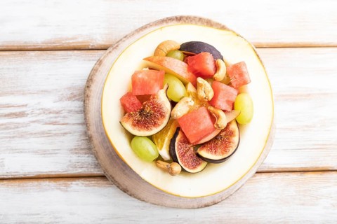 Vegetarian fruit salad of watermelon, grapes, figs, pear, orange, cashew on white wooden background