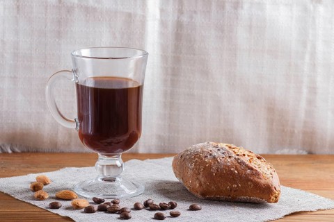 Glass cup of coffee with bun on a wooden background and linen textile. close up, copy space