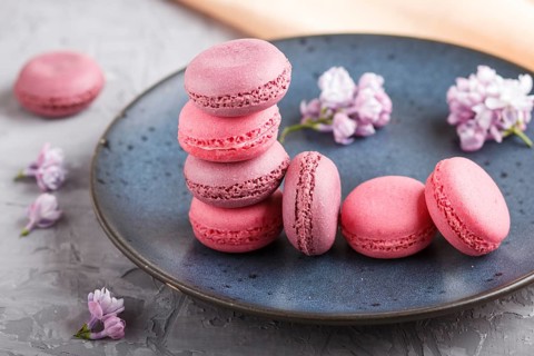 Purple and pink macaron or macaroon cakes with lilac flowers on blue ceramic plate on a gray