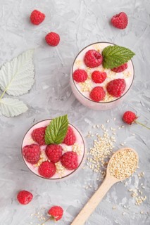 Yoghurt with raspberry and sesame in a glass and wooden spoon on gray concrete background. top