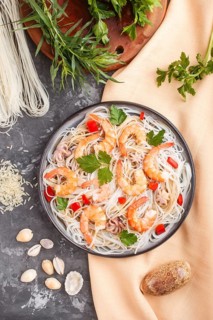 Rice noodles with shrimps or prawns and small octopuses on gray ceramic plate on a black concrete