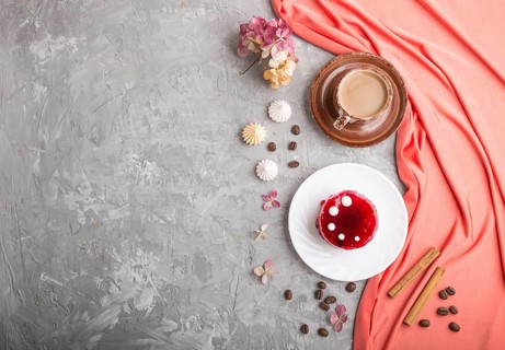 Red cake with souffle cream with cup of coffee on a gray concrete background and red textile. top