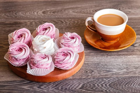Pink and white marshmallows (zephyr) on a round wooden board with cup of coffee on a gray wooden