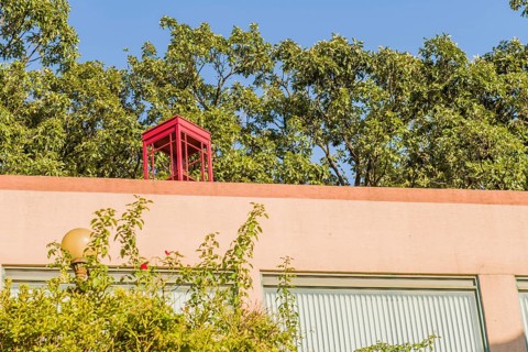 Red wooden telephone booth without glass on top of pink stucco building on sunny day with blue sky
