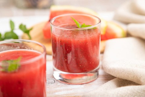 Watermelon juice with chia seeds and mint in glass on a white wooden background with linen textile.