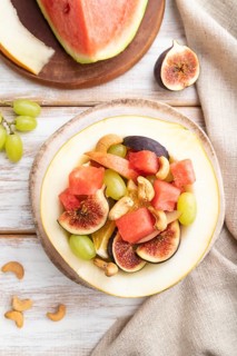 Vegetarian fruit salad of watermelon, grapes, figs, pear, orange, cashew on white wooden background