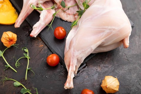 Whole raw rabbit with pumpkin, tomatoes, pea sprouts on a black concrete background and linen