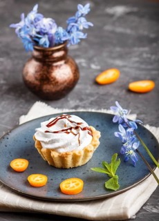 Cake with whipped egg cream on a blue ceramic plate with kumquat slices and mint leaves on a black