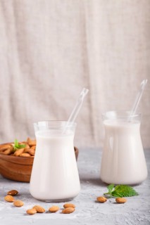 Organic non dairy almond milk in glass and wooden plate with almond nuts on a gray concrete