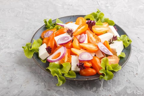 Vegetarian salad with fresh grape tomatoes, feta cheese, lettuce and onion on blue ceramic plate on