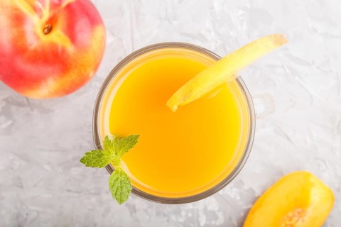 Glass of peach juice on a gray concrete background. Morninig, spring, healthy drink concept. Top