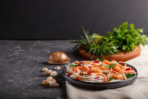 Rice noodles with shrimps or prawns and small octopuses on gray ceramic plate on a black concrete