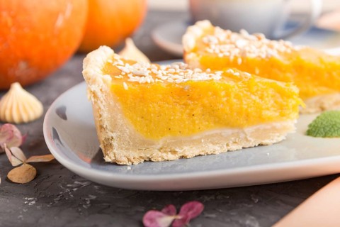 Two pieces of traditional american pumpkin pie with cup of coffee on a black concrete background