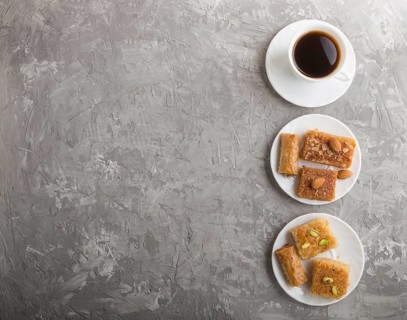 Traditional arabic sweets (basbus, kunafa, baklava) on white plate and a cup of coffee on a gray