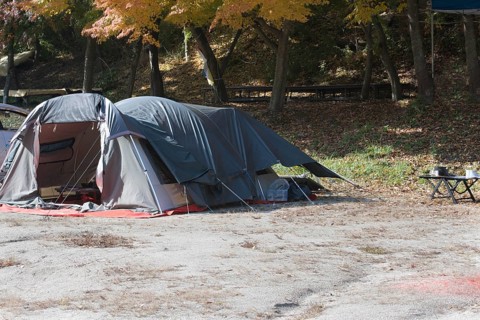 Camping tent set up in mountain park on sunny fall day with cooking pans on small wooden table in