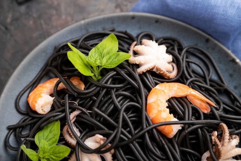 Black cuttlefish ink pasta with shrimps or prawns and small octopuses on black concrete background