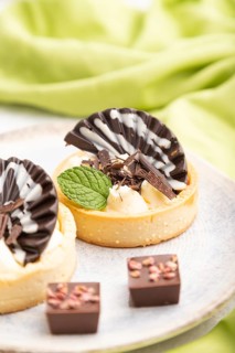Sweet tartlets with chocolate and cheese cream with cup of coffee on a gray concrete background and