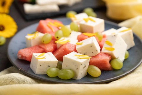 Vegetarian salad with watermelon, feta cheese, and grapes on blue ceramic plate on black concrete