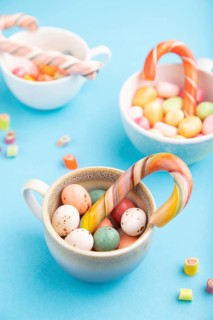 Heap of multicolored caramel candies in cups on blue pastel background. close up, side view,