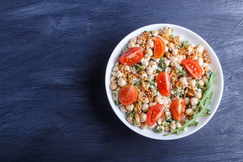 Vegetarian salad of boiled chickpeas, cheese, arugula, mustard and cherry tomatoes on black wooden