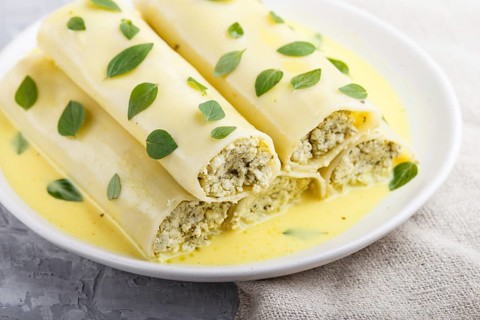 Cannelloni pasta with egg sauce, cream cheese and oregano leaves on a gray concrete background with