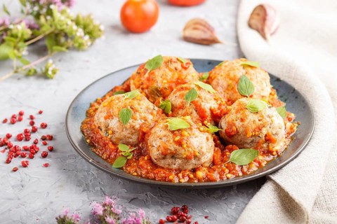 Pork meatballs with tomato sauce, oregano leaves, spices and herbs on blue ceramic plate on a gray