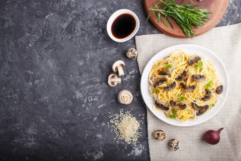 Rice noodles with champignons mushrooms, egg sauce and oregano on white ceramic plate on a black