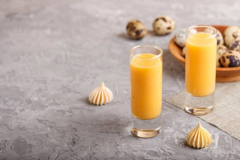 Sweet egg liqueur in glass with quail eggs and meringues on a gray concrete background. Side view,