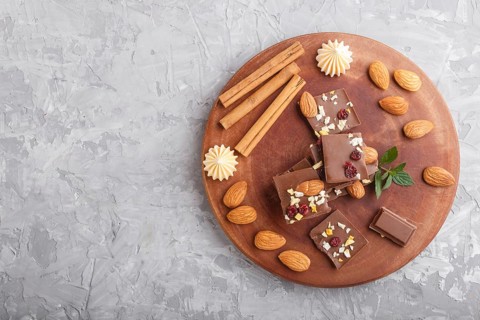 A pieces of milk chocolate with almonds and dried fruits on a brown wooden board on a gray concrete