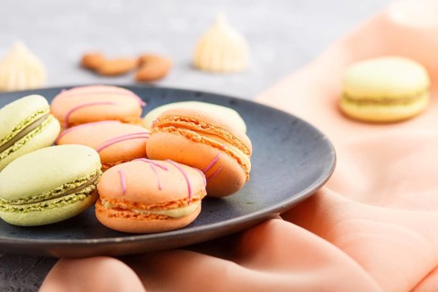 Orange and green macarons or macaroons cakes on blue ceramic plate on a gray concrete background.